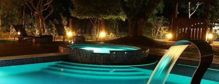 Piscina iluminada à noite com cascata em inox