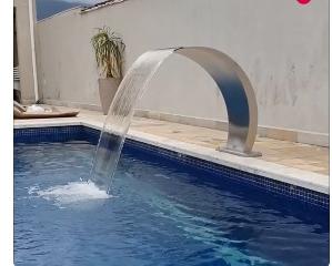 Cascata em inox, bica em arco alta, instalada na borda da piscina